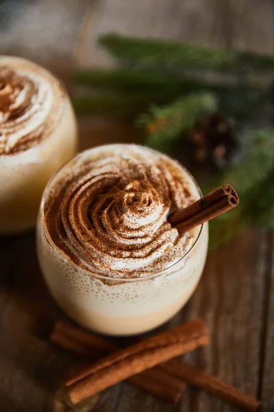 Vista de cerca de delicioso cóctel de ponche de huevo con crema batida y canela en la mesa de madera - foto de stock