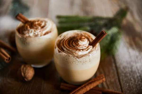 Selective focus of delicious eggnog cocktail with whipped cream near cinnamon sticks on wooden table — Stock Photo