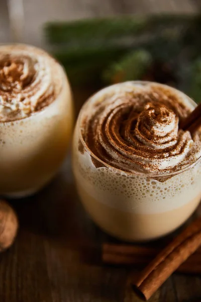Vue rapprochée de savoureuse boisson au lait de poule avec crème fouettée et cannelle sur table en bois — Photo de stock