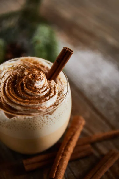 Close up view of flavored eggnog drink with whipped cream on wooden table near cinnamon sticks — Stock Photo