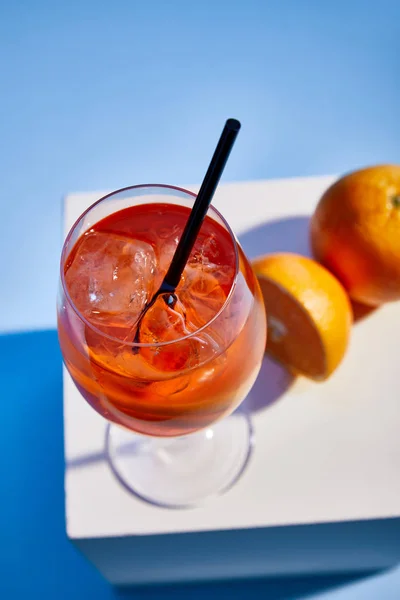 Vista de alto ángulo de cóctel Aperol Spritz con paja en vidrio y naranjas sobre fondo azul - foto de stock