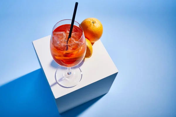 Vista de alto ângulo de cocktail Aperol Spritz com palha em vidro e laranjas sobre fundo azul — Fotografia de Stock