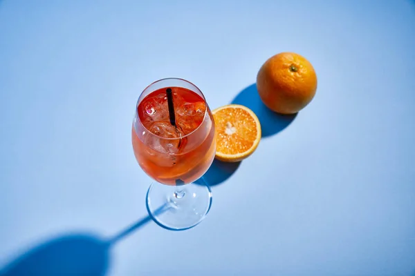 Высокий угол обзора коктейля Aperol Spritz с соломой в стекле и апельсинами на синем фоне — стоковое фото