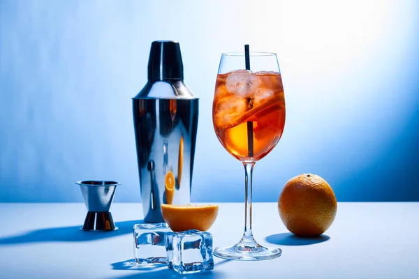 Cocktail Aperol Spritz, oranges, shaker, ice cubes and measuring cup on blue background — Stock Photo