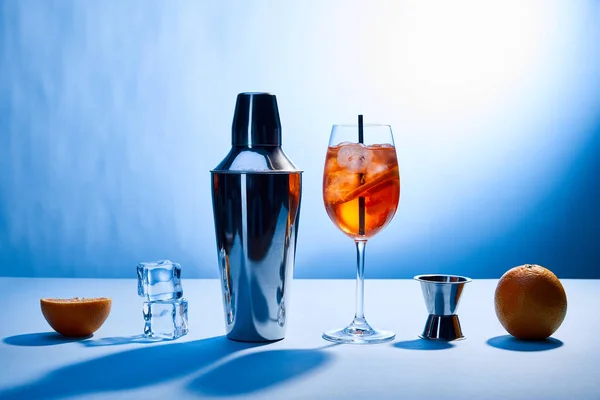 Cocktail Aperol Spritz, oranges, shaker, ice cubes and measuring cup on blue background — Stock Photo