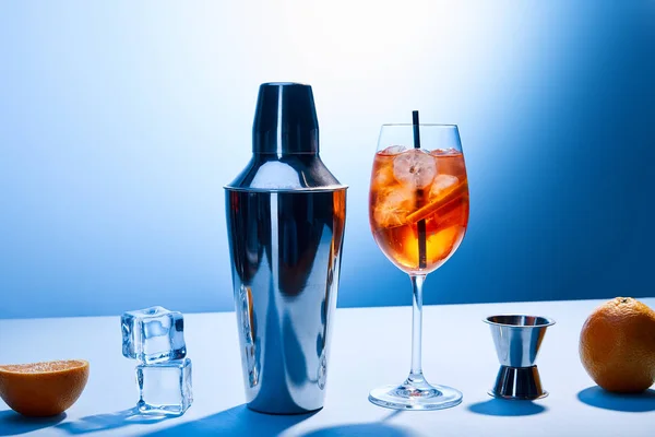 Cocktail Aperol Spritz, arance, shaker, cubetti di ghiaccio e misurino su fondo blu — Foto stock
