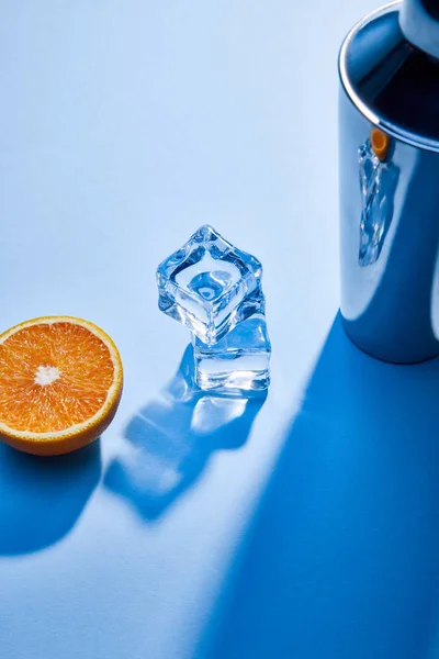 Vista de ángulo alto de naranja, agitador, cubitos de hielo sobre fondo azul - foto de stock