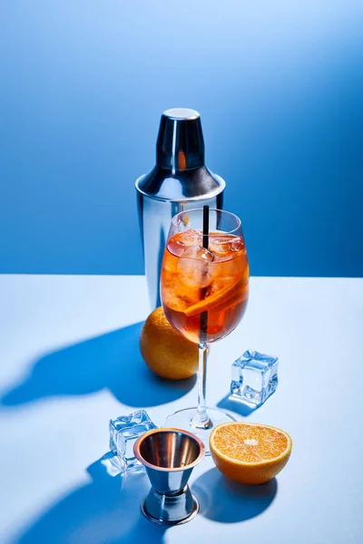 Коктейль Aperol Spritz, апельсины, шейкер, кубики льда и измерительная чашка на синем фоне — стоковое фото