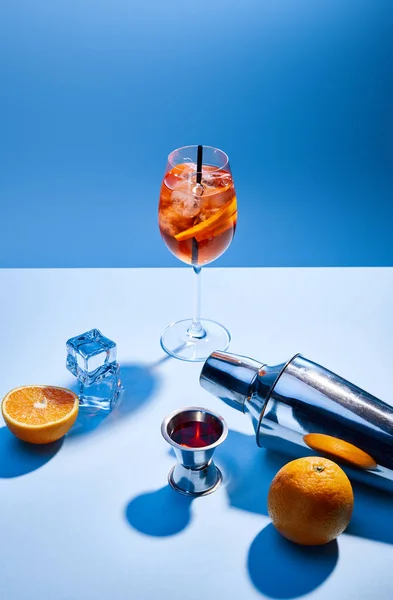 Aperol Spritz, oranges, shaker, glaçons et tasse à mesurer sur fond bleu — Photo de stock