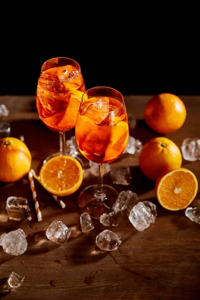 High angle view of Aperol Spritz in glasses, oranges and ice cubes on black background — Stock Photo