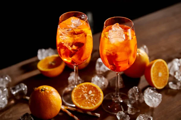 Vista de alto ángulo de Aperol Spritz en vasos, naranjas y cubitos de hielo sobre fondo negro - foto de stock