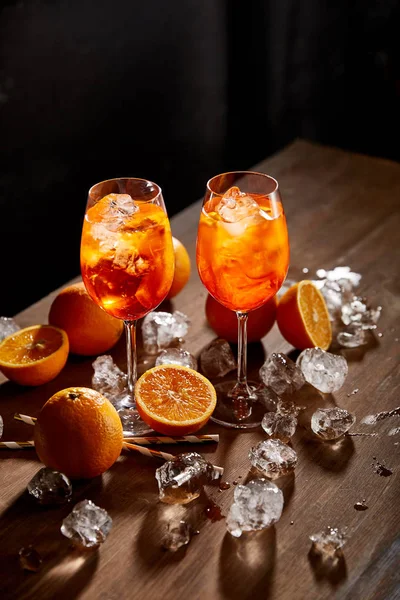 Aperol Spritz in glasses, oranges and ice cubes on black background — Stock Photo