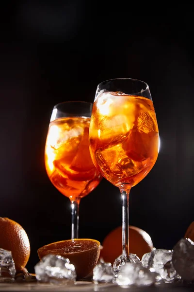 Aperol Spritz in glasses, oranges and ice cubes on black background — Stock Photo