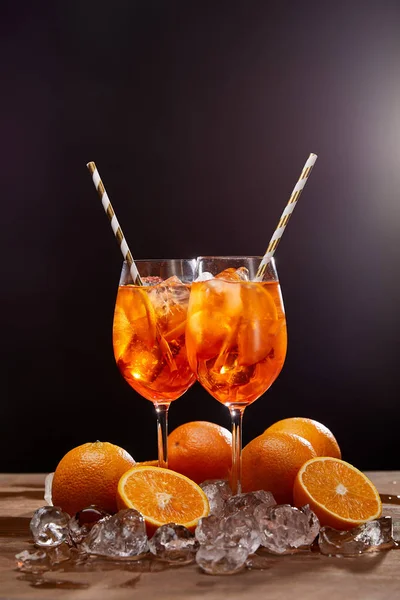 Aperol Spritz in glasses, oranges and ice cubes on black background — Stock Photo