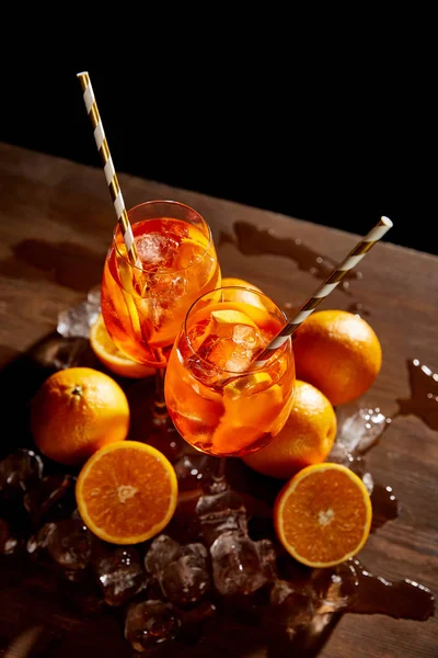 Високий кут огляду Aperol Spritz в окулярах, апельсинах і кубиках льоду на чорному тлі — Stock Photo