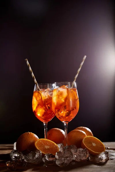 Aperol Spritz in glasses, oranges and ice cubes on black background — Stock Photo