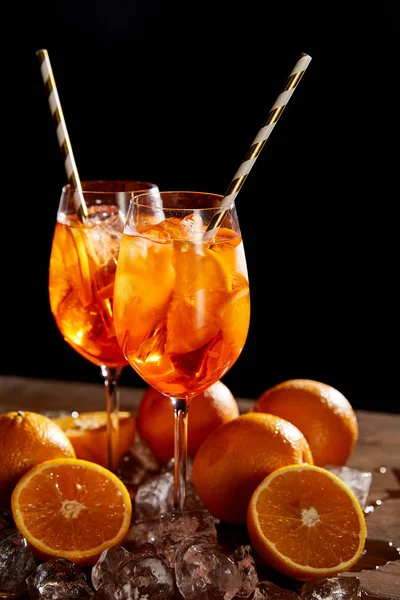 Aperol Spritz em copos, laranjas e cubos de gelo sobre fundo preto — Fotografia de Stock