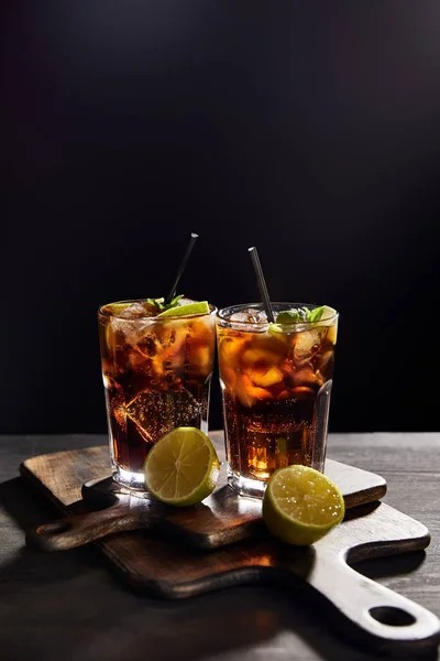 Cocktails cuba libre in glasses with straws and limes on black background — Stock Photo