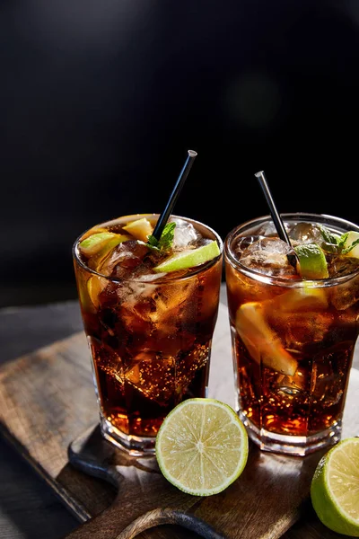 Cocktails cuba libre in glasses with straws and limes on black background — Stock Photo