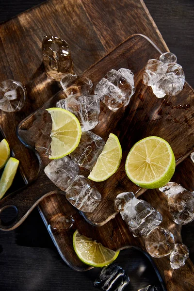 Vista superior de cubitos de hielo y limas cortadas en tablas de cortar de madera - foto de stock