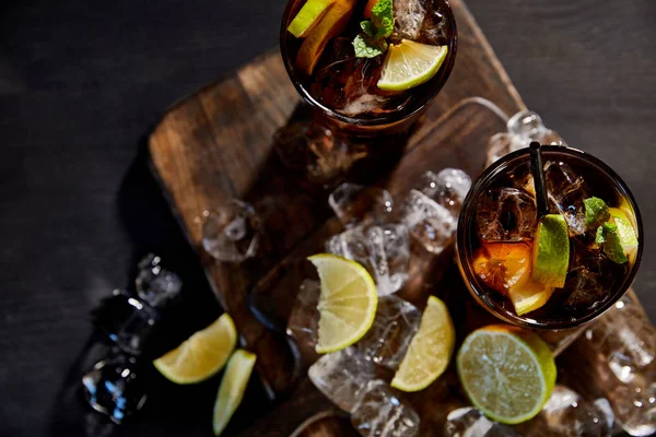 Вид на коктейли куба либр в стаканах с соломинками, кубиками льда и лаймами на черном фоне — стоковое фото