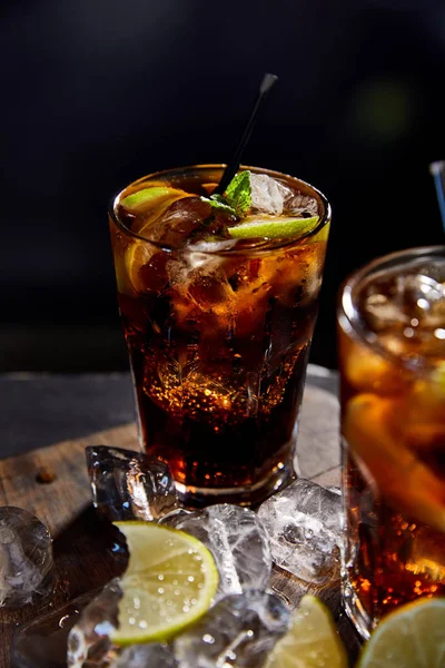 Foyer sélectif de cocktails cuba libre dans des verres avec des pailles, des glaçons et des citrons verts sur fond noir — Photo de stock