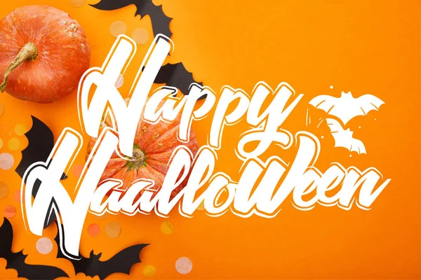 Vue de dessus de citrouille, chauves-souris et confettis sur fond orange avec illustration heureuse Halloween — Photo de stock