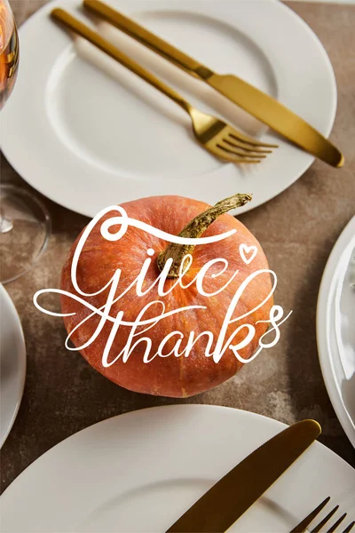Whole ripe pumpkin with give thanks illustration near white plates with golden knives and forks on stone table — Stock Photo