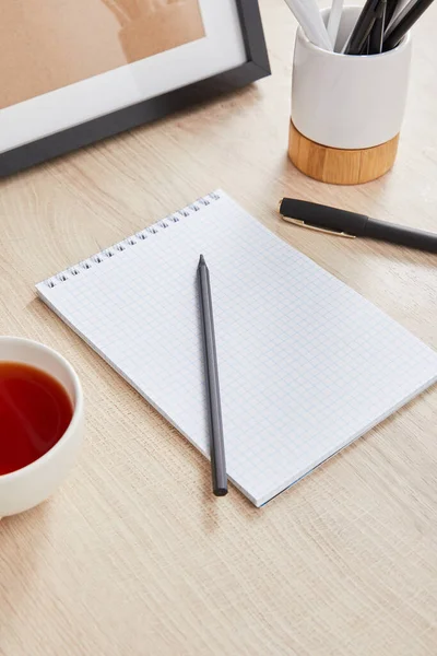 Cup of tea and blank notebook with pencil and pen on wooden surface — Stock Photo