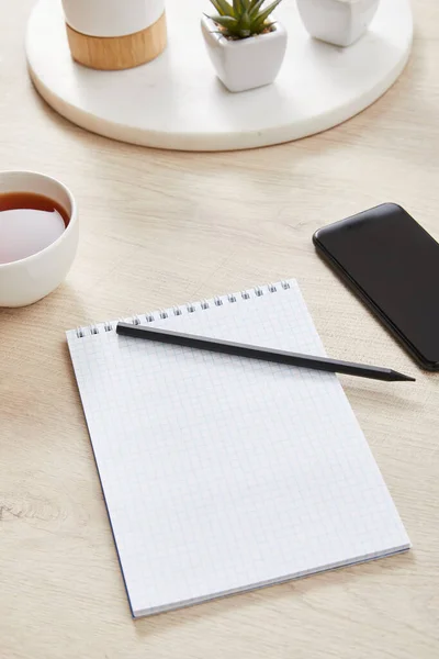 Grüne Pflanze, Tasse Tee und leeres Notizbuch mit Bleistift in der Nähe von Smartphone auf Holzoberfläche — Stockfoto