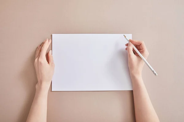 Vista recortada de la mujer escribiendo en papel con lápiz sobre superficie beige - foto de stock