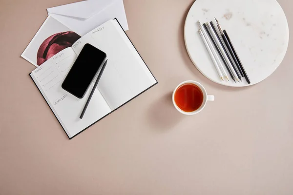 Vue du dessus de tasse de thé, enveloppe, planificateur, carte, smartphone près du cercle avec crayons sur la surface beige — Photo de stock