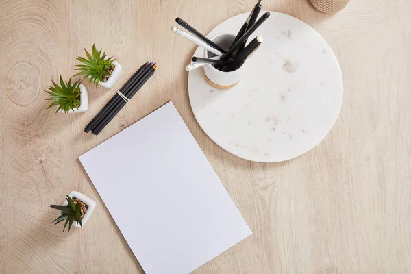 Top view of green plants, colored pencils near white paper and stone board with holder on wooden surface — Stock Photo