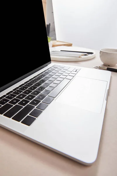 Laptop mit leerem Bildschirm bei Tasse Tee und Schreibwaren auf beiger Oberfläche — Stockfoto