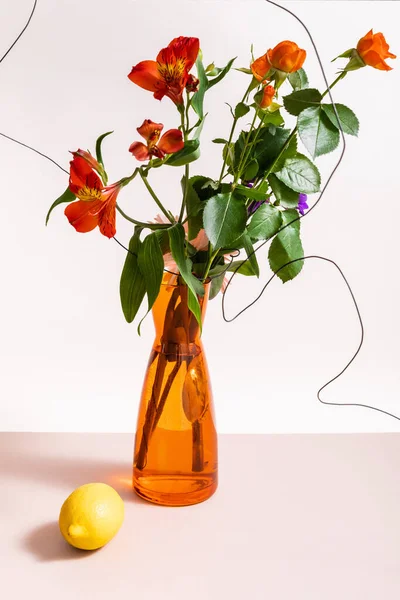 Квіткова композиція з трояндами і червоними альстромеріями в дротах у помаранчевій вазі біля лимона ізольовані на білому — стокове фото