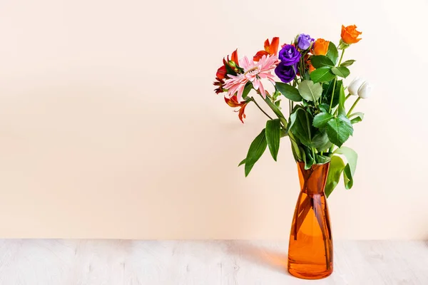 Floral composition with bouquet in orange vase on wooden surface on beige background — Stock Photo