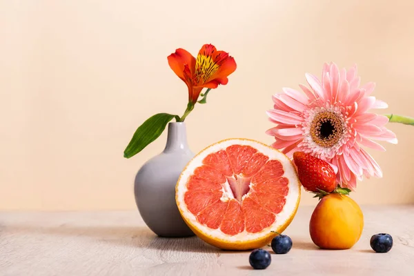 Цветочный и фруктовый состав с альстромерией, герберой, ягодами, грейпфрутом и абрикосом на деревянной поверхности, изолированной на бежевом — стоковое фото