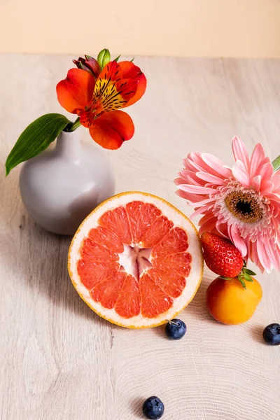 Квіткова і фруктова композиція з альстромеріями, герберою, ягодами, грейпфрутом і абрикосом на дерев'яній поверхні ізольовані на бежевому — стокове фото