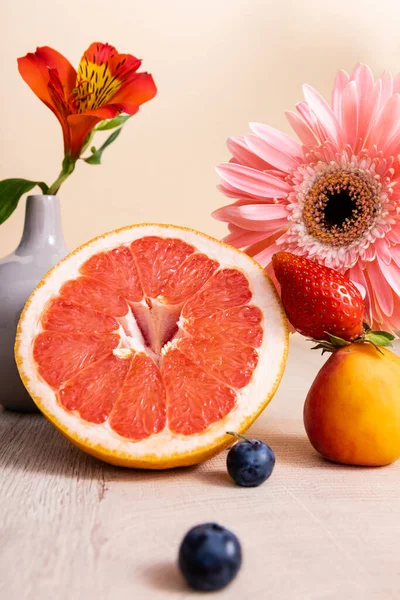 Floral and fruit composition with Alstroemeria, gerbera, berries, grapefruit and apricot on wooden surface isolated on beige — Stock Photo