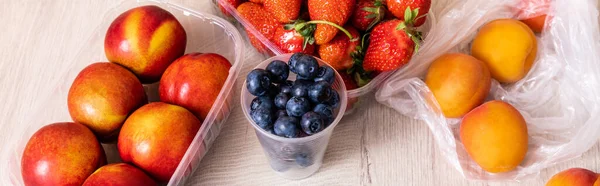 Composición de frutas con arándanos, fresas, nectarinas y melocotones en envases de plástico sobre superficie de madera, cultivo panorámico - foto de stock