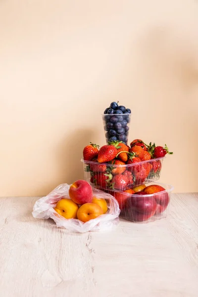 Composição de frutos com mirtilos, morangos, nectarinas e pêssegos em recipientes de plástico sobre superfície de madeira sobre fundo bege — Fotografia de Stock