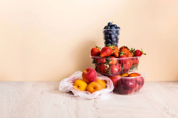 Composizione di frutta con mirtilli, fragole, pesche noci e pesche in contenitori di plastica su superficie di legno su fondo beige — Foto stock