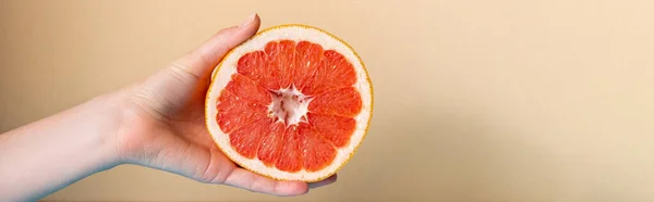 Cropped view of female hand with juicy grapefruit half on beige background, panoramic crop — Stock Photo