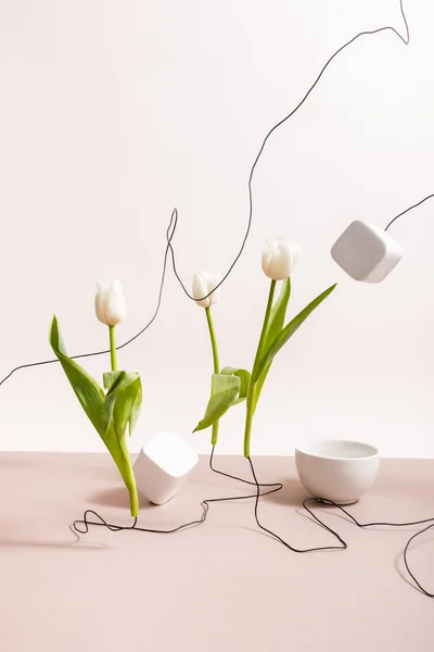 Composición floral creativa con tulipanes en cables, taza y cubos cuadrados aislados en beige - foto de stock