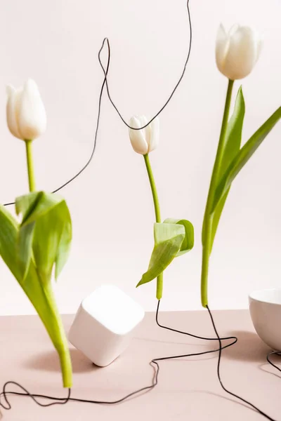 Селективный фокус творческой цветочной композиции с тюльпанами на проволоке, чашке и квадратном кубе, изолированном на бежевом — стоковое фото
