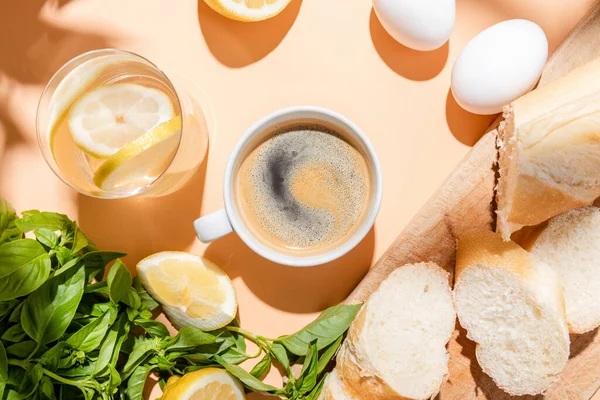 Blick von oben auf Kaffee, Wasser, Eier und Baguette zum Frühstück auf beigem Tisch — Stockfoto