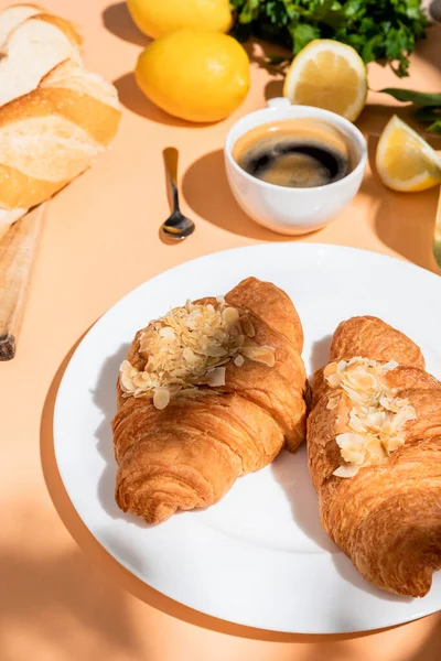 Croissants, baguette, limones y taza de café para el desayuno en la mesa beige - foto de stock