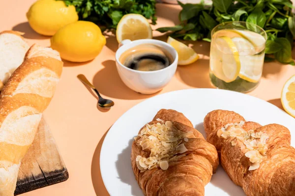 Cruasanes frescos, baguette, limones y taza de café para el desayuno en la mesa beige - foto de stock