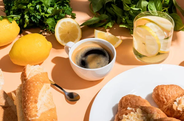 Kaffee, frische Croissants und Wasser zum Frühstück auf beigem Tisch — Stockfoto