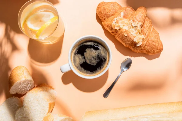 Blick von oben auf Kaffee, Wasser, Baguette und Croissant zum Frühstück auf beigem Tisch — Stockfoto
